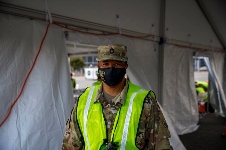 A member of the Delaware National Guard poses under a TentCraft drive-thru tent used for a mobile COVID-19 vaccination clinic.” style=