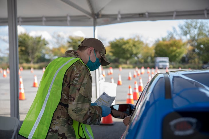 Member of the Delaware National Guard speaks with a member of the public during a drive-thru COVID-19 vaccine clinic.”