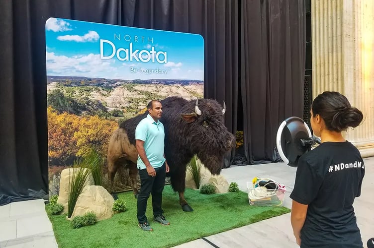 Man stands in front of a photo bacdrop for a North Dakota tourism organization