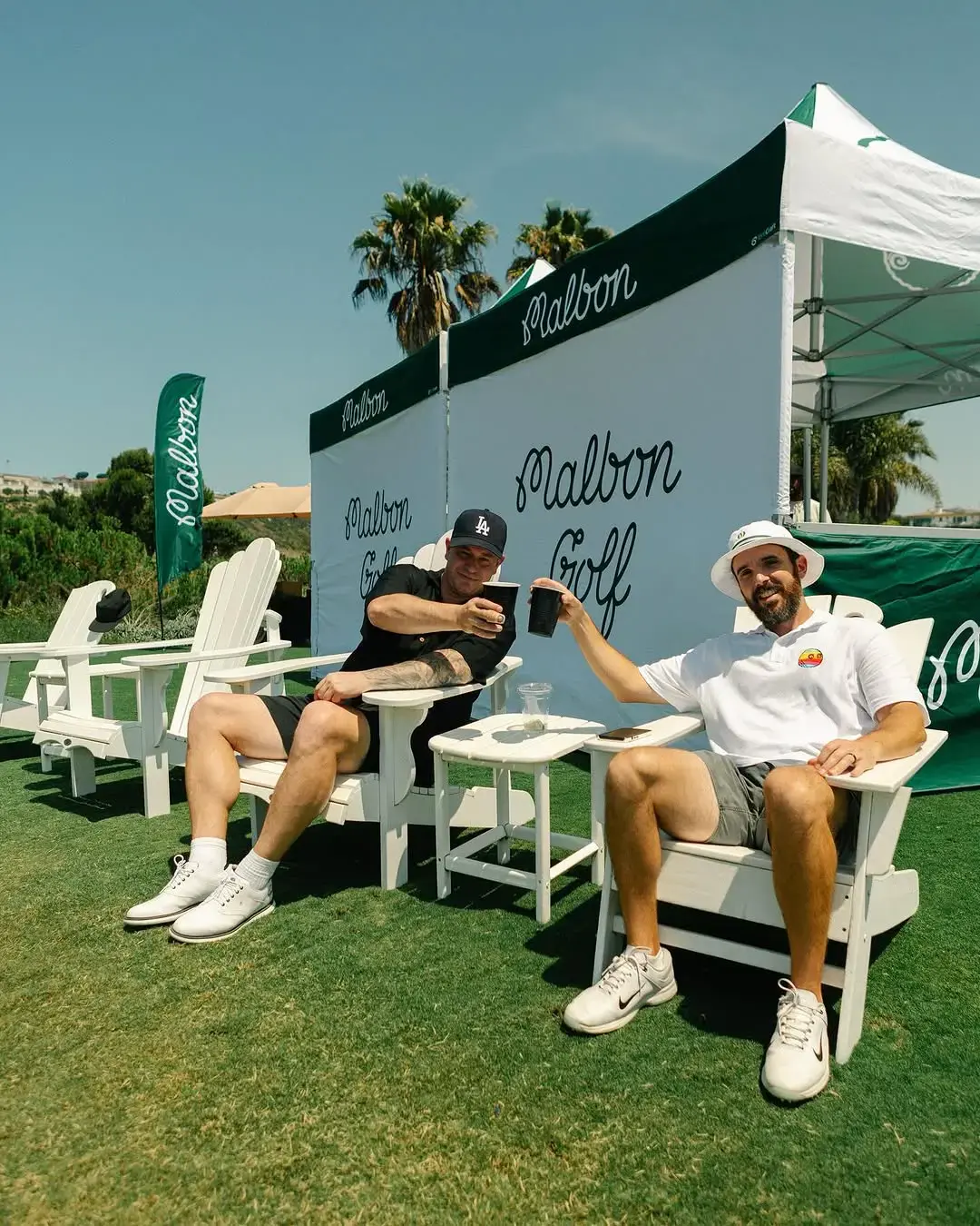 A pair of golfers cheers by a Malbon Golf tent at a tournament