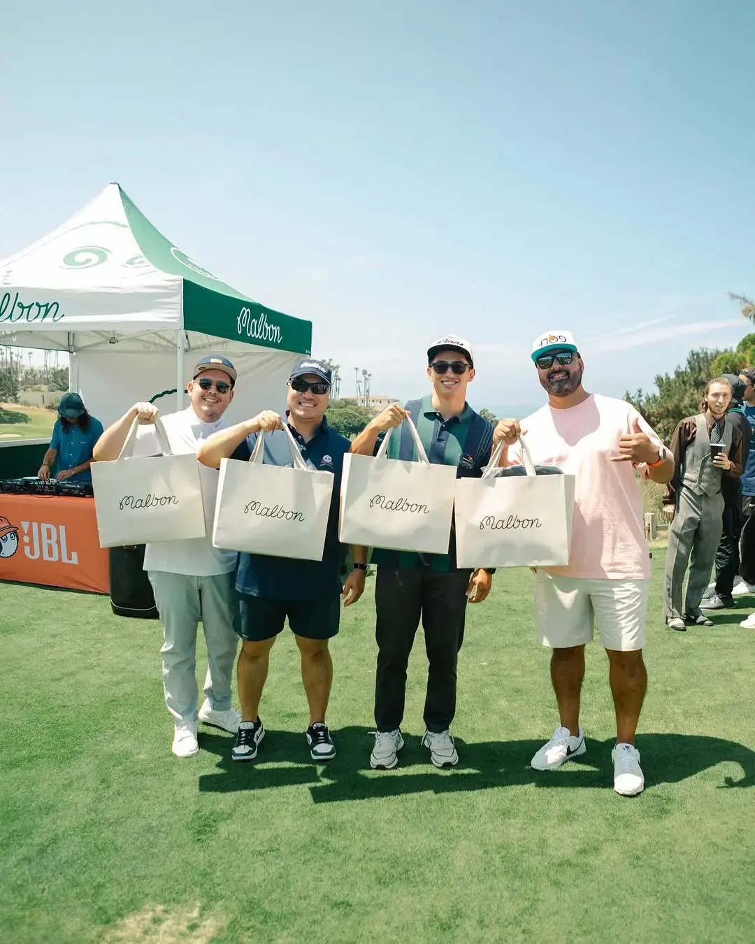 Four golfers pose with shopping bags in front of Malbon Buckets Club Tent